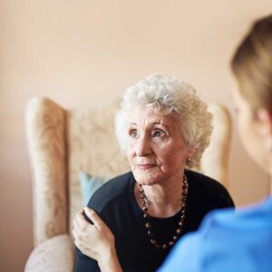 Older adult choosing clothing with a caregiver in a bright private assisted living room.